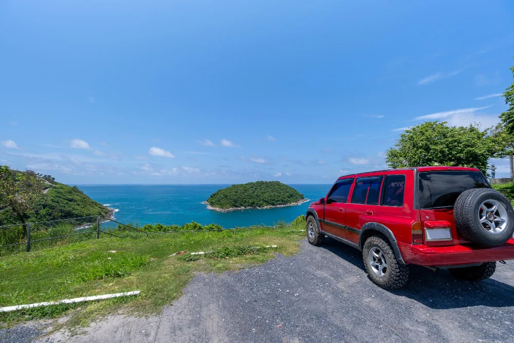 Red 4x4 rental car parked on a coastal road overlooking a small Bahamian island